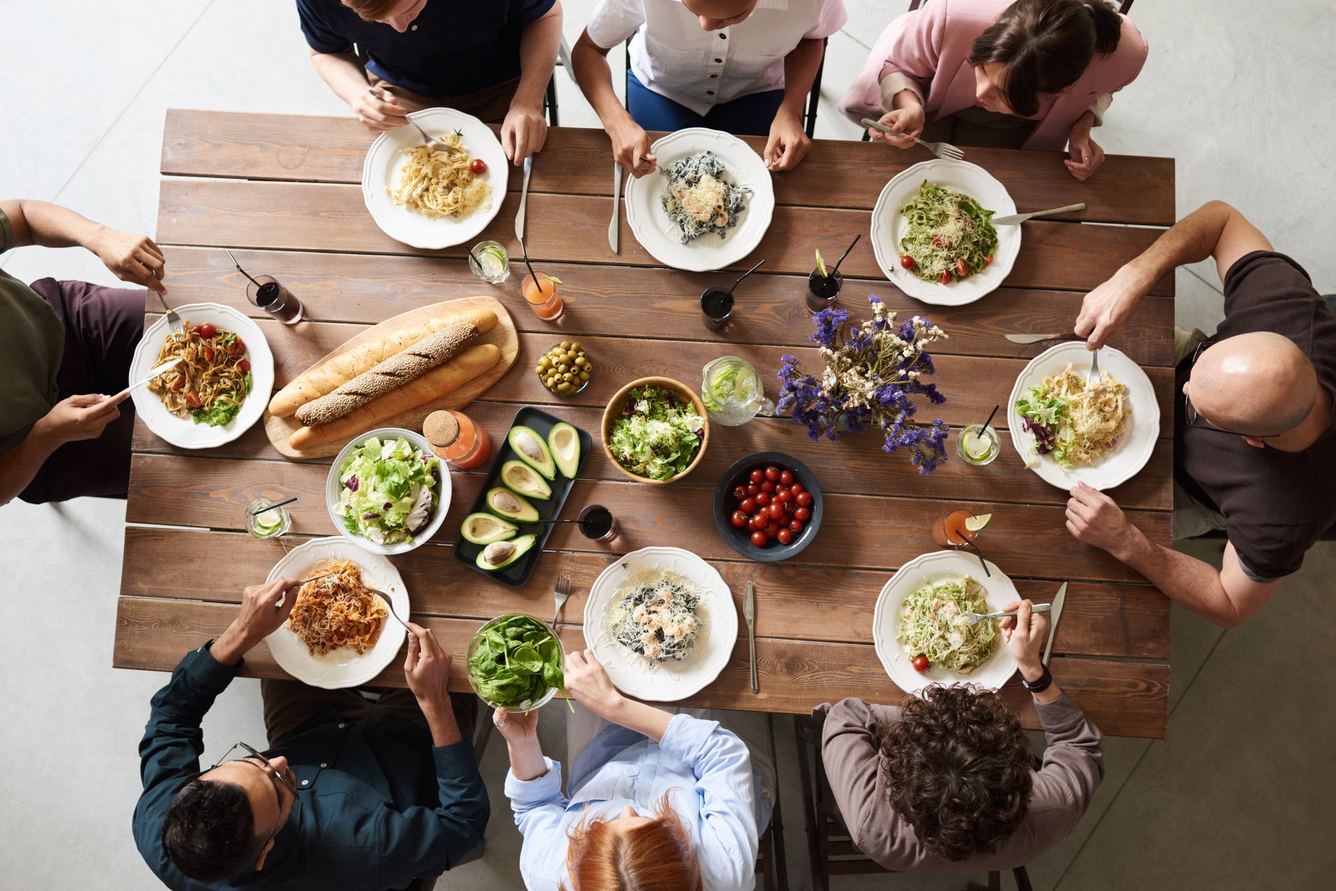 Eight people around a restaurant table with shared dishes, seen from above