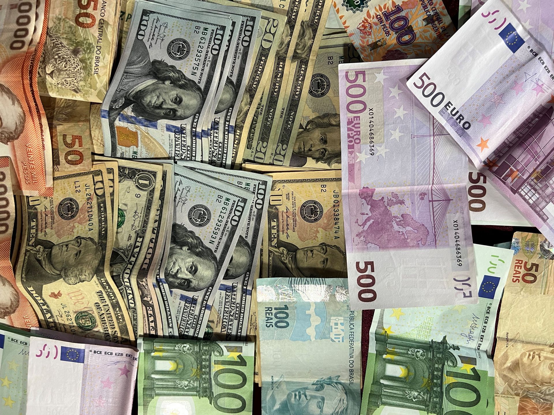 Banknotes from several countries piled together and overlapping, including US dollars, euros and Brazilian reais