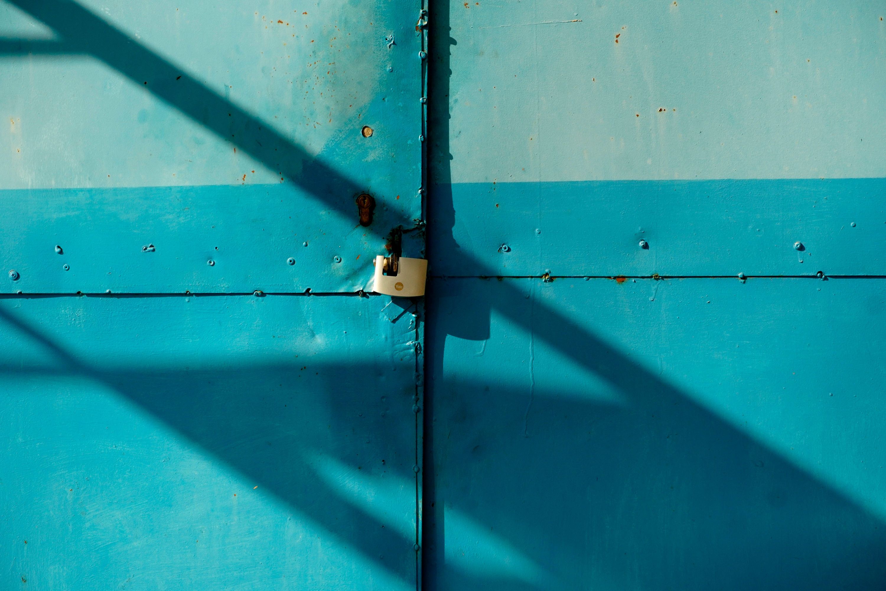 A padlock hanging on the bolt of a teal painted metal gate in hard sunlight